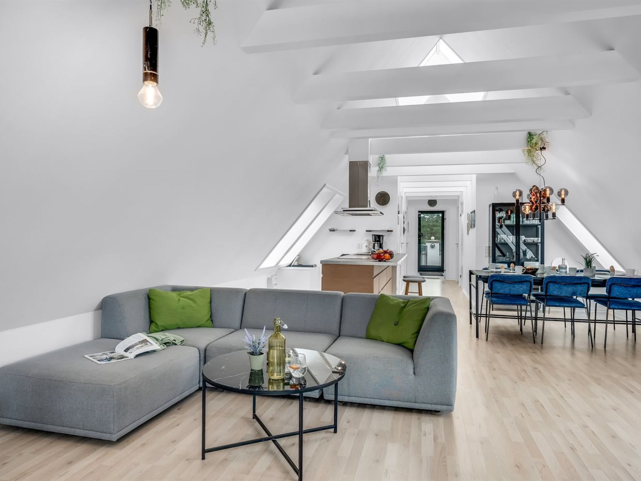 A modern living room with a grey sectional sofa, a round coffee table, and a dining area with blue chairs.