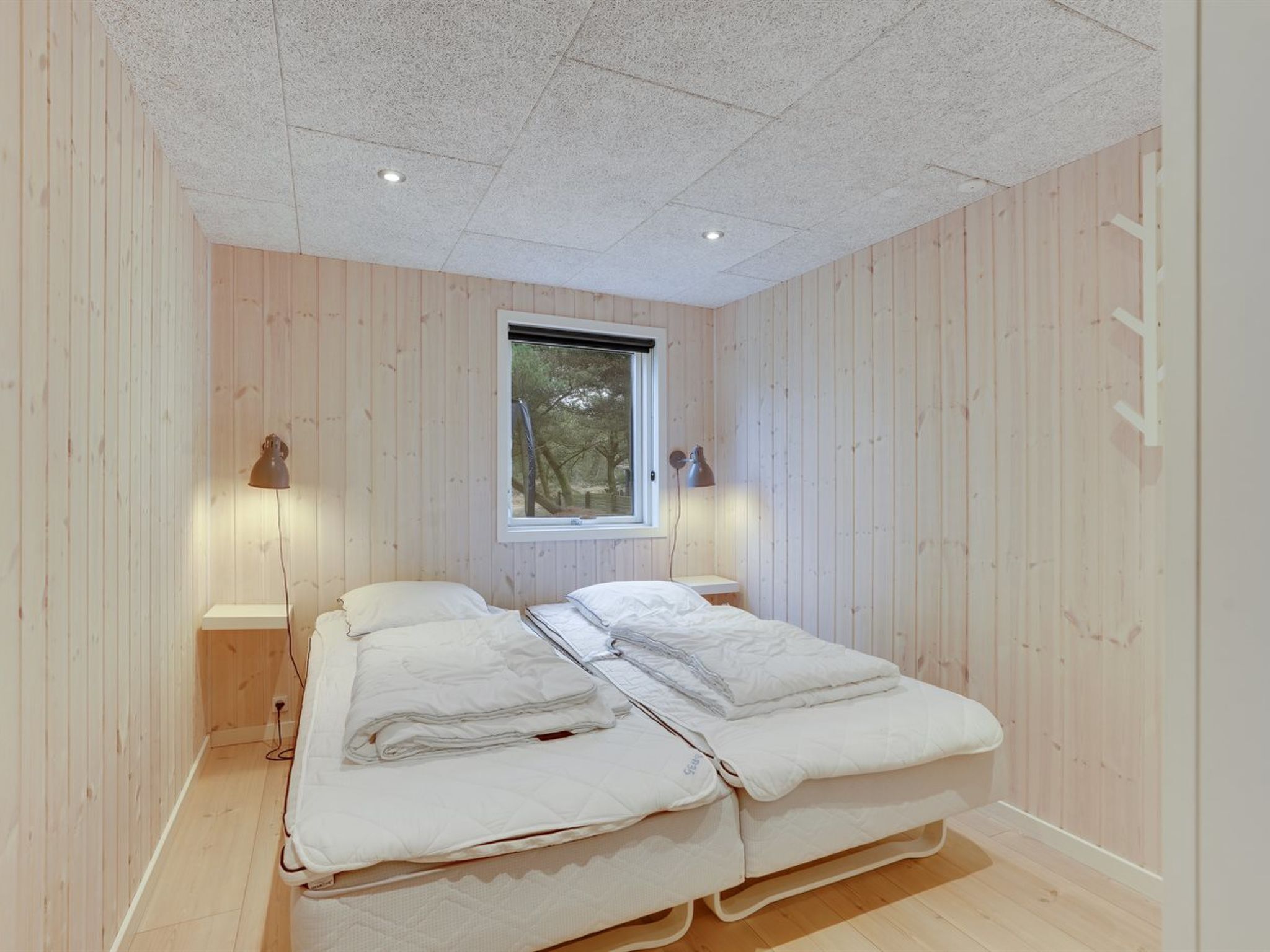 A bedroom with two beds, wooden walls, a window, and two bedside lamps.