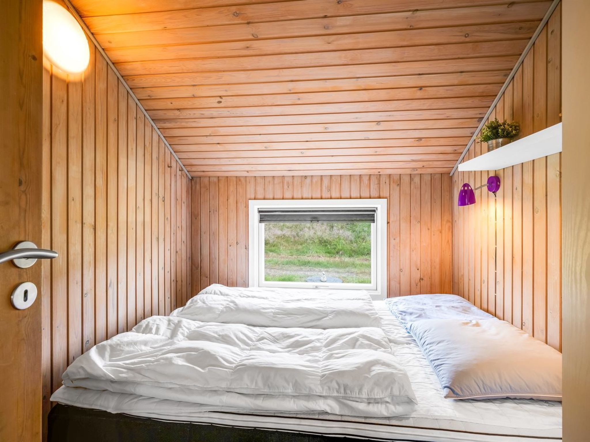 A wooden-paneled room with a bed, a window, and a door.