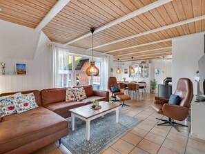 Un grand espace de vie doté d’un plafond en bois, d’un ensemble de canapés, d’une table à manger et d’un coin cuisine.
