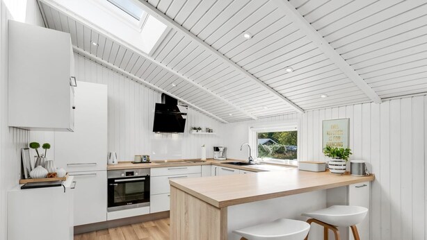 Eine moderne Küche mit weißen Schränken, einer Holzinsel mit Barhocker, einem eingebauten Ofen und einem großen Fenster für natürliches Licht.