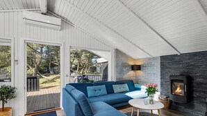 Ein modernes Wohnzimmer mit einem blauen Ecksofa, einem Kamin und Blick ins Freie.