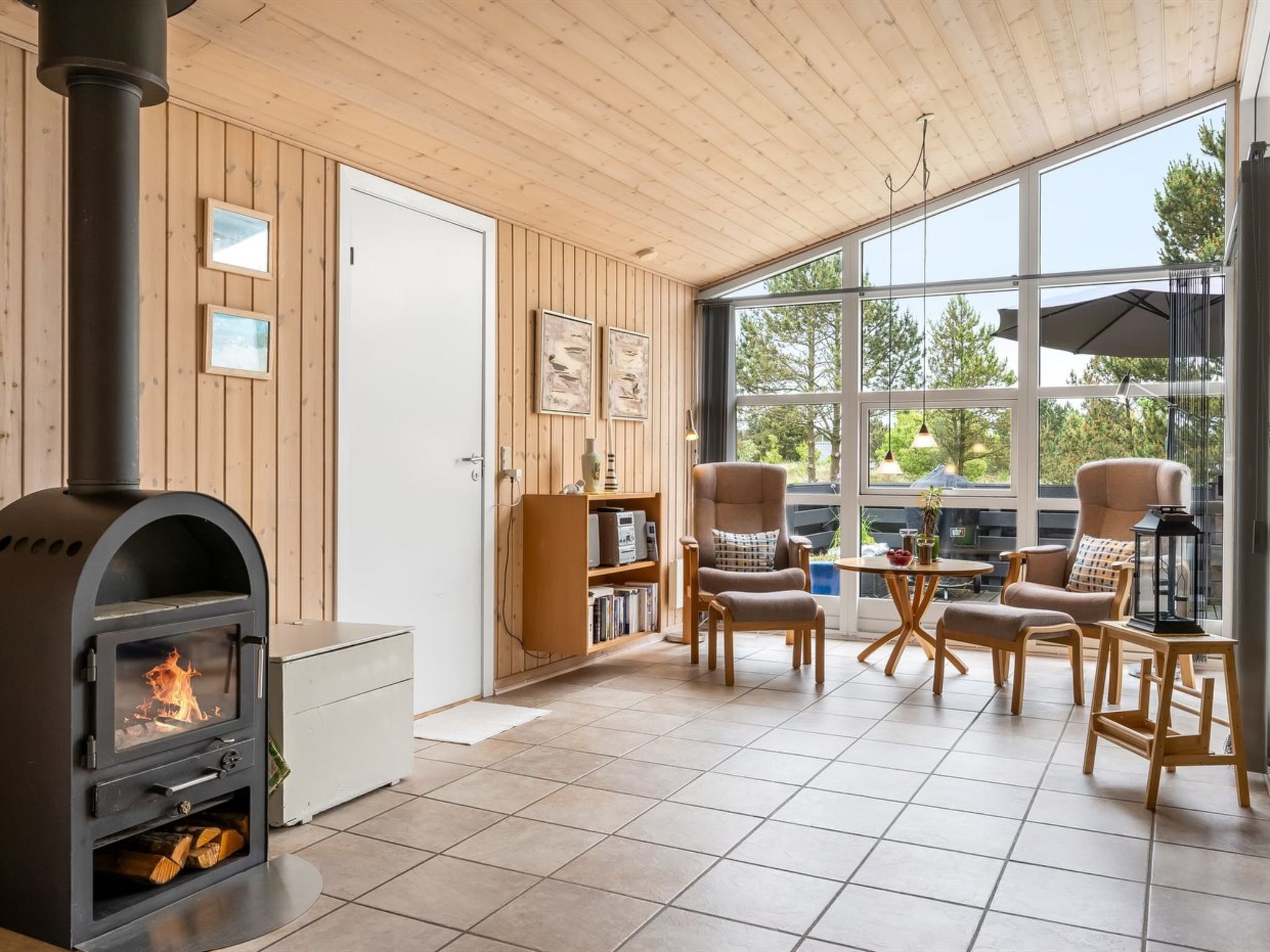 Una habitación acogedora con estufa de leña, paredes de madera, ventanas amplias y un mobiliario cómodo.