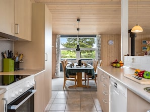 A modern kitchen with wooden cabinets, a dining table, and a view of greenery outside.