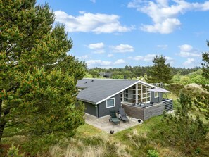A modern house with a large deck, surrounded by trees and grassy areas.