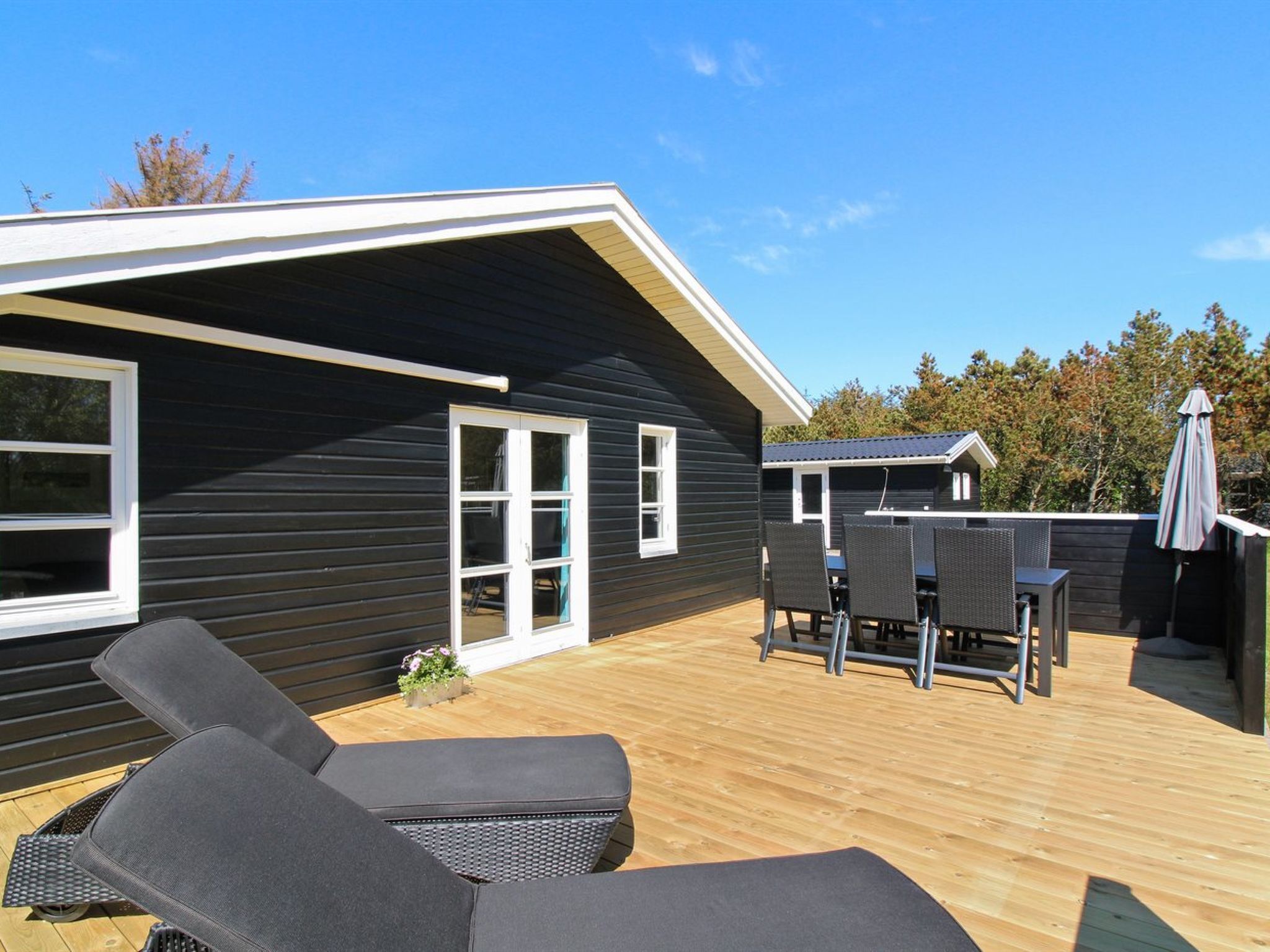 A modern house with a deck, two lounge chairs, and a dining table.