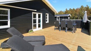 A modern house with a deck, two lounge chairs, and a dining table.