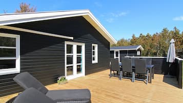 A modern house with a deck, two lounge chairs, and a dining table.