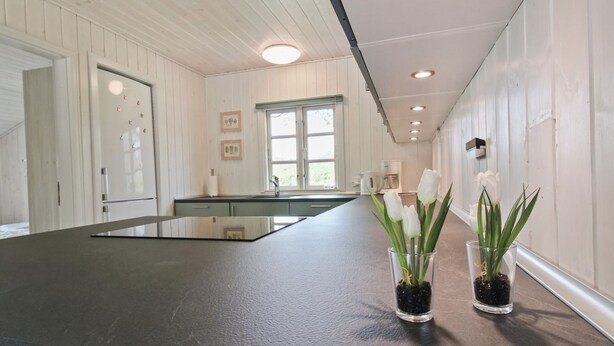 A kitchen with a dark countertop, white cabinetry, and a window with a view. There are two glass vases with white flowers on the countertop.