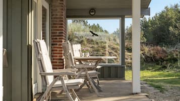 A covered outdoor area with wooden deck, lounge chairs, and a picnic table.