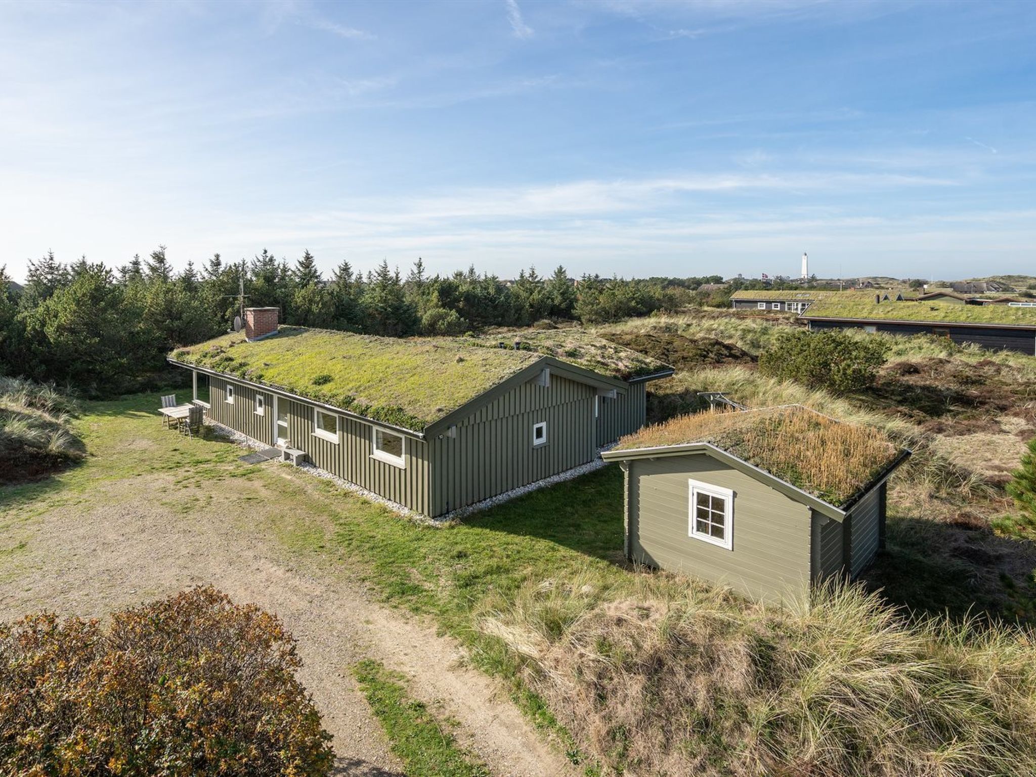 Una casa con techo verde, un cobertizo pequeño adosado y un sendero de grava que conduce a la casa.