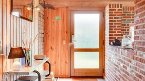 A wooden interior with a glass door, a brick wall, and a small table with a lamp and decorative items. - "Neja" - 400m from the sea by Interhome (Blåvand)
