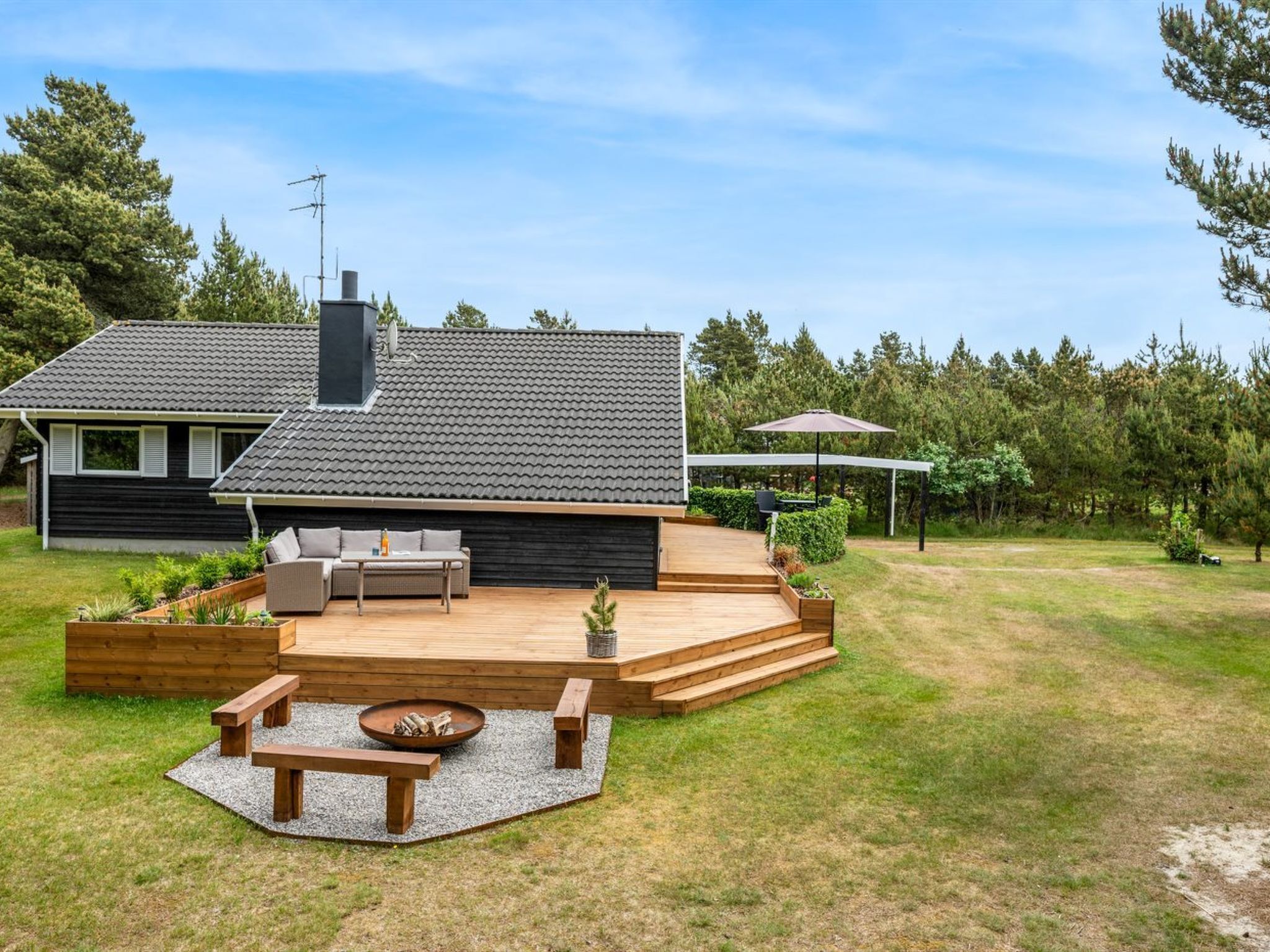 Ein modernes Haus mit einer Terrasse, Sitzgelegenheiten im Freien und einer Feuerstelle.
