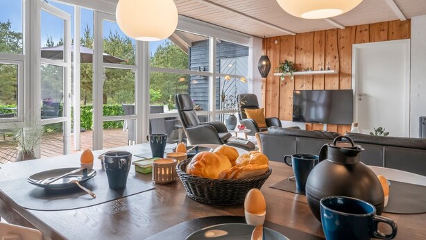A modern kitchen with a dining area, large windows, and a TV.