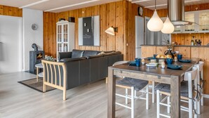 A modern kitchen with wooden walls, a dining area with a wooden table and chairs, and a built-in stove.