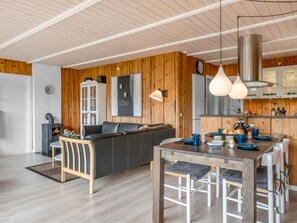 Una cocina moderna con paredes de madera, un comedor con mesa y sillas de madera, y una estufa empotrada.