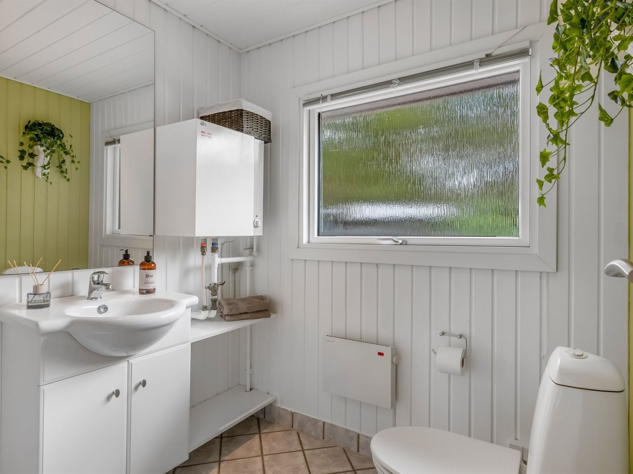 A bathroom with a white sink, mirror, and toilet, a window with a view, and a radiator.