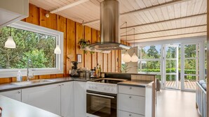 A modern kitchen with wooden walls, a large window, and a view of greenery.
