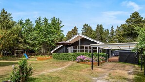 A modern house with a covered patio, a play area with a slide, and a garden with flowering plants.