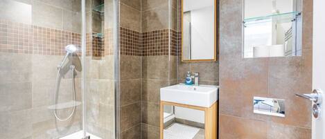 Un baño moderno con cabina de ducha de vidrio, lavamanos con espejo y un inodoro.