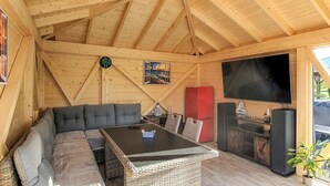 A cozy wooden cabin interior with a sofa, a table, a clock, a painting, and a TV. - Ferienwohnung Neppermin/Usedom (Neppermin/Usedom)