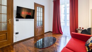 Un salon moderne avec un canapé rouge, une table basse en marbre noir et un téléviseur affichant le logo de Netflix.