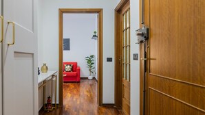 Un couloir avec une porte en bois, un canapé rouge, une plante en pot et une petite table sur laquelle se trouve un vase.