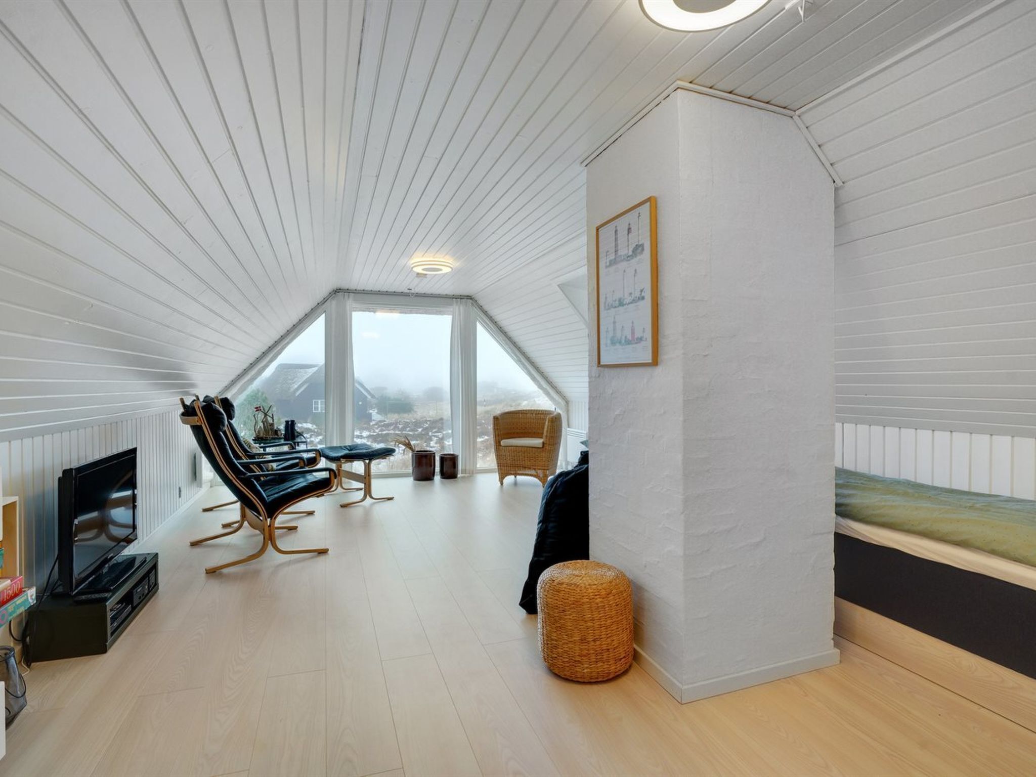 A spacious attic room with a high ceiling, large windows, a flat-screen TV, and a cozy seating area with a sofa and chairs.