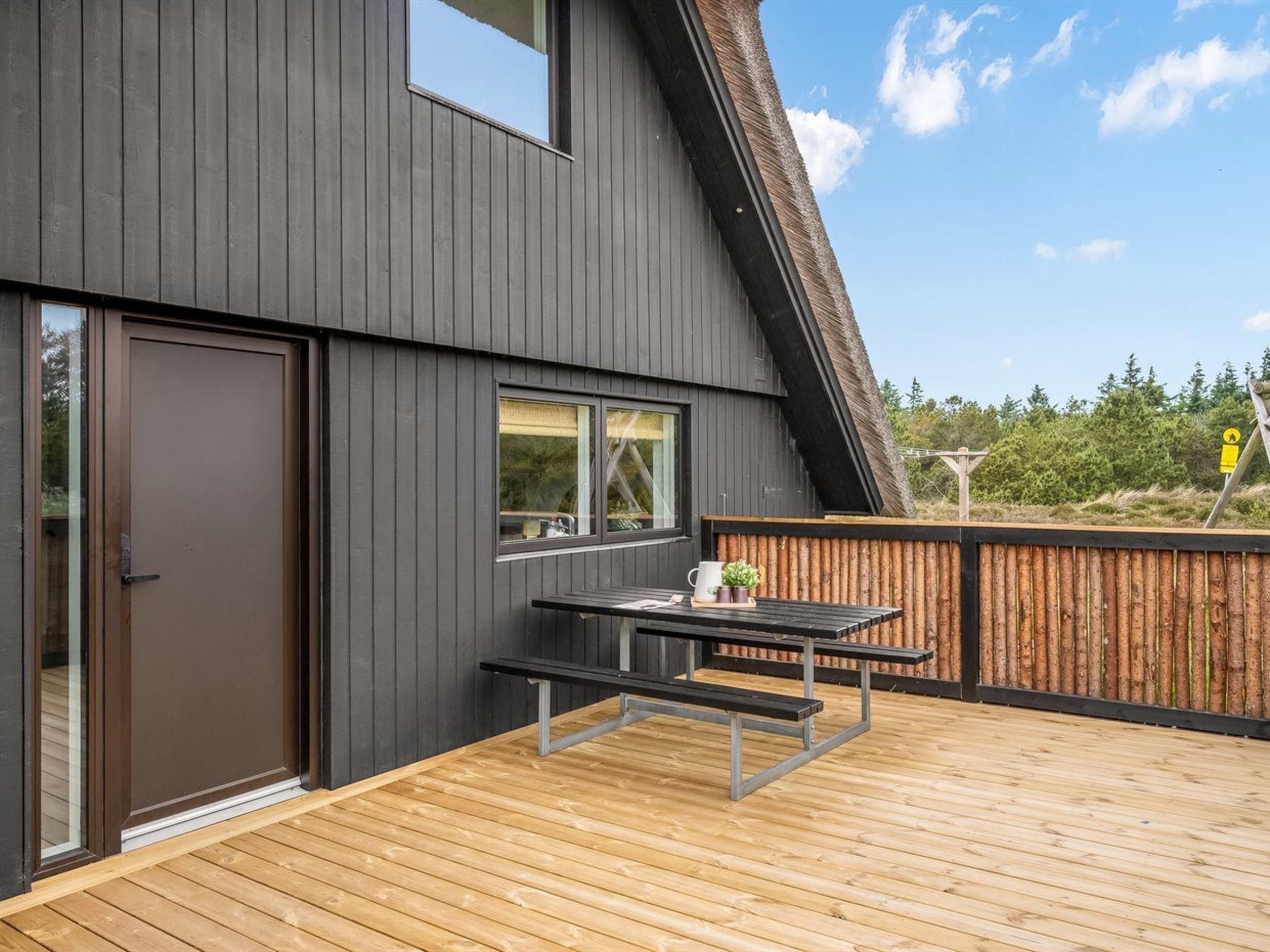A modern building with a wooden deck, a bench, and a table with outdoor seating.