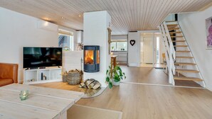Een moderne woonkamer met een open haard, een televisie en een trap die naar een andere kamer leidt.