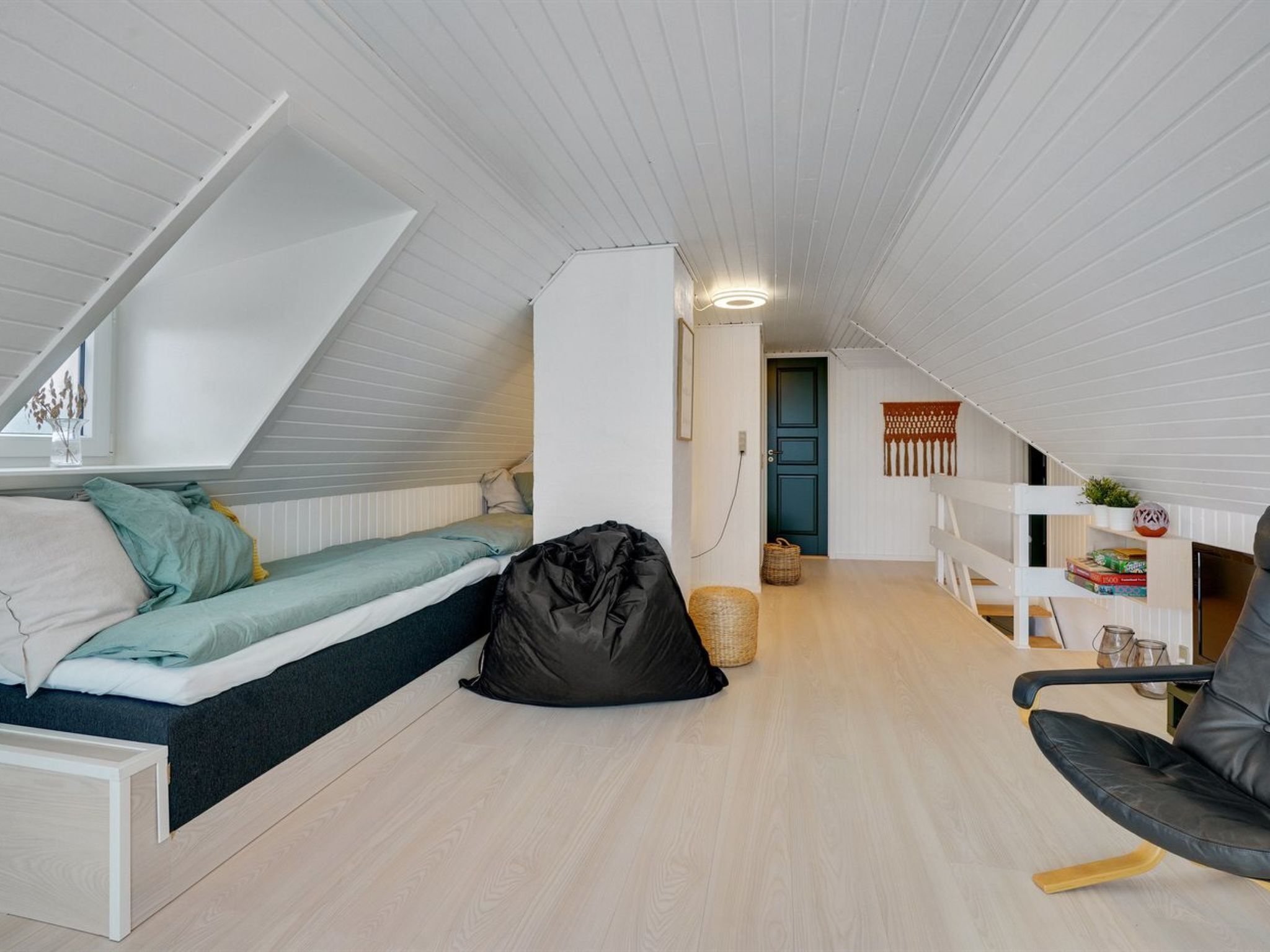 A small, well-lit attic bedroom with a bunk bed, a desk, and a chair.