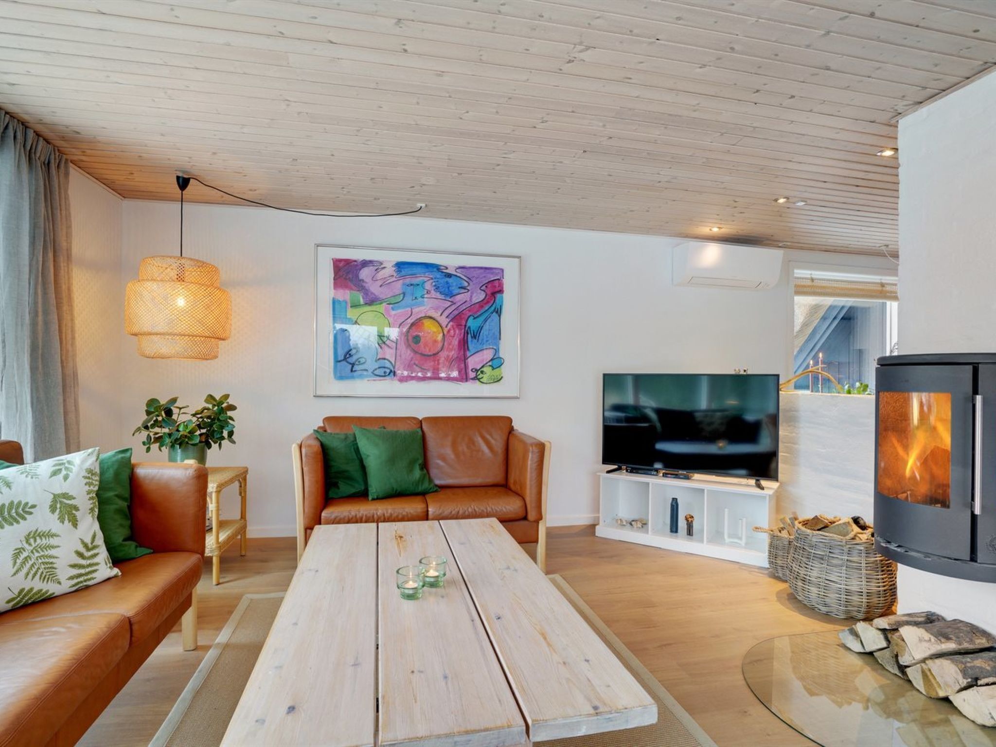 A modern living room with a wooden ceiling, a brown leather sofa, a wooden coffee table, a TV, and a fireplace.