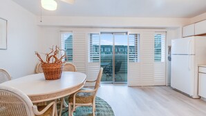 Une cuisine moderne avec un réfrigérateur blanc, une table à manger entourée de chaises en osier et un ventilateur de plafond.