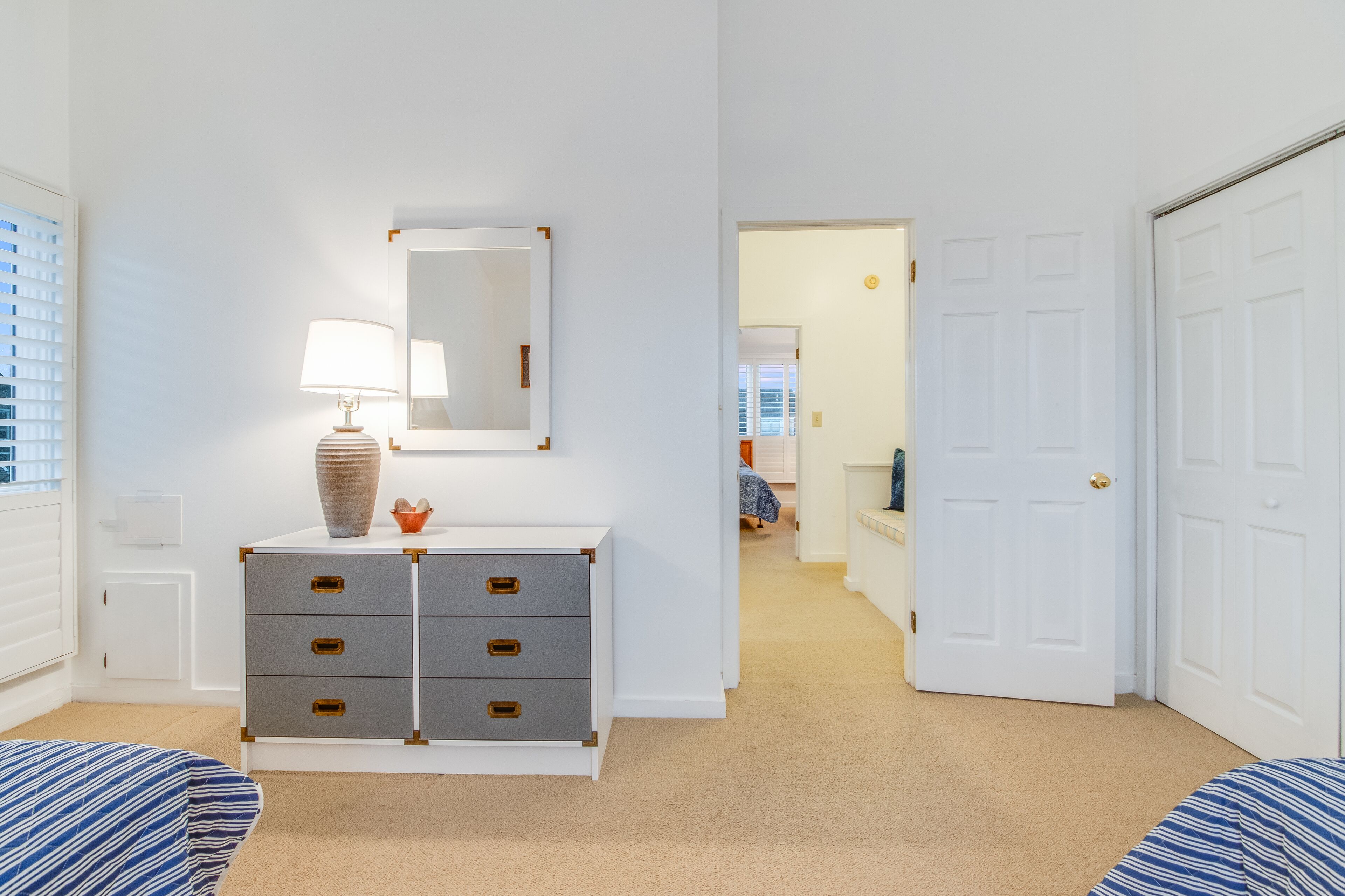 Une chambre à coucher comprenant un lit, une commode, un miroir et une porte donnant sur une autre pièce.