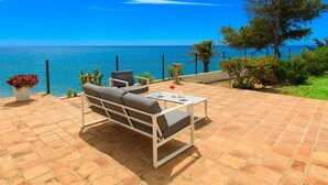 Une terrasse avec vue sur la mer, un canapé, une table et des plantes en pot.