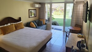 Ein Hotelzimmer mit einem großen Bett, einer Couch, einem Esstisch und Blick auf den Garten.