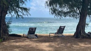 Zwei Strandstühle mit Blick auf das Meer, Bäume bilden den Rahmen.