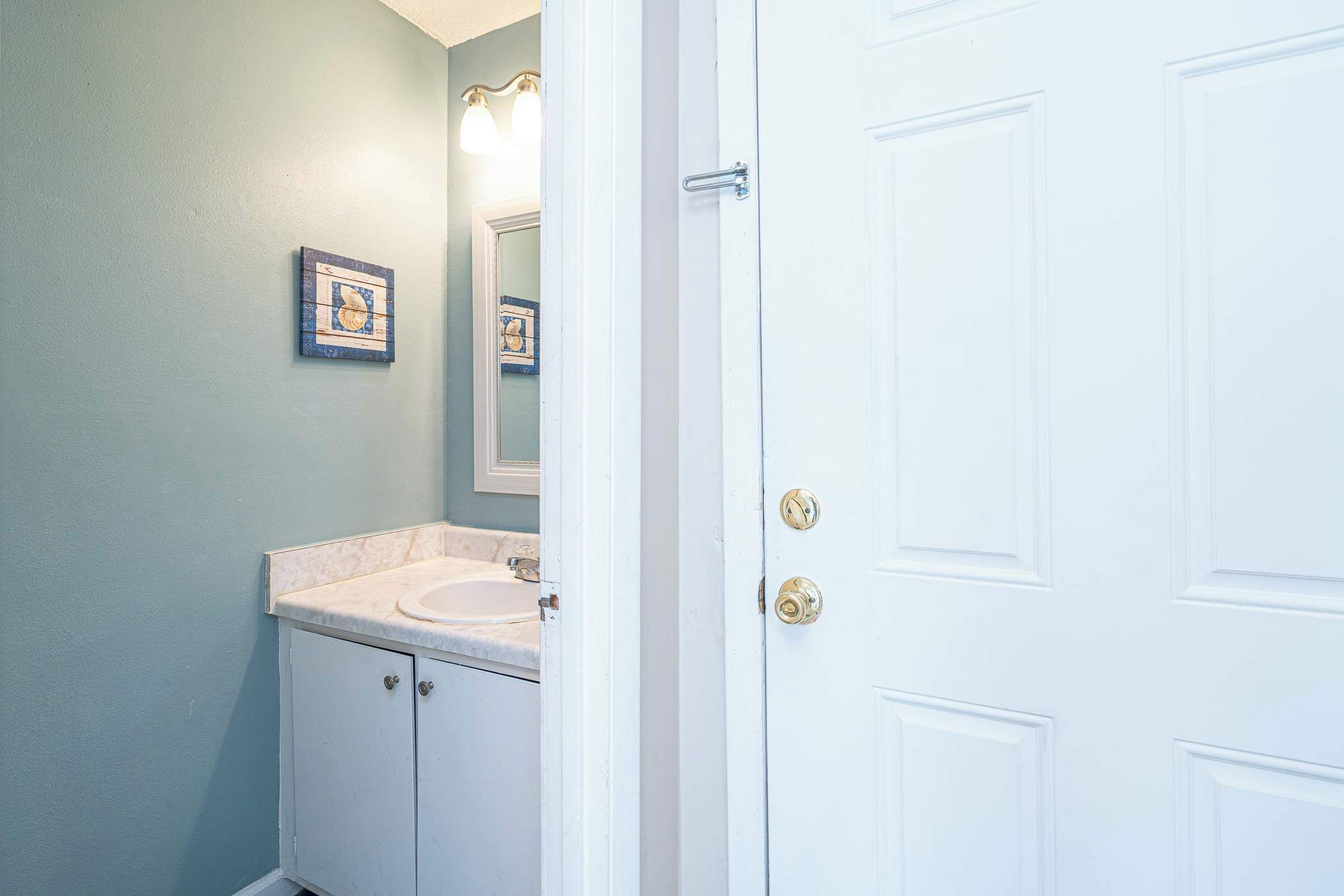 A bathroom with a white sink, a mirror, and a door with a handle.