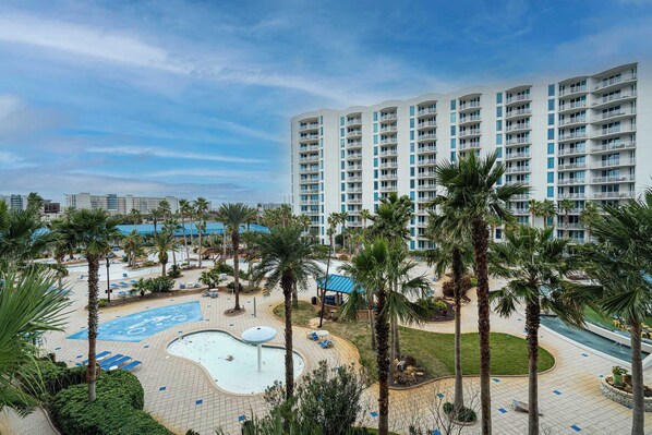 Un hotel con una amplia zona de piscina, palmeras y un edificio moderno con balcones.