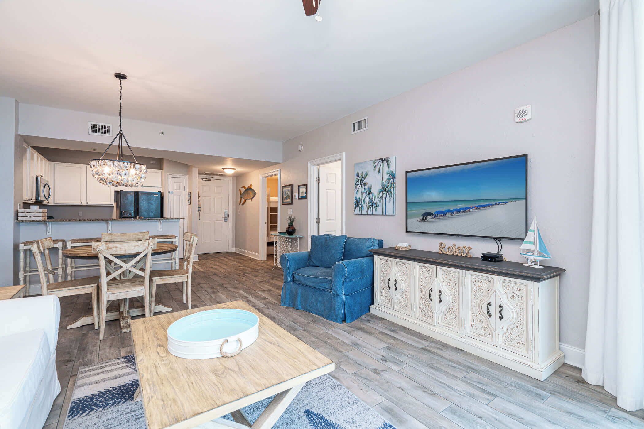 A spacious living area with a dining table, blue armchair, and a large TV on the wall.