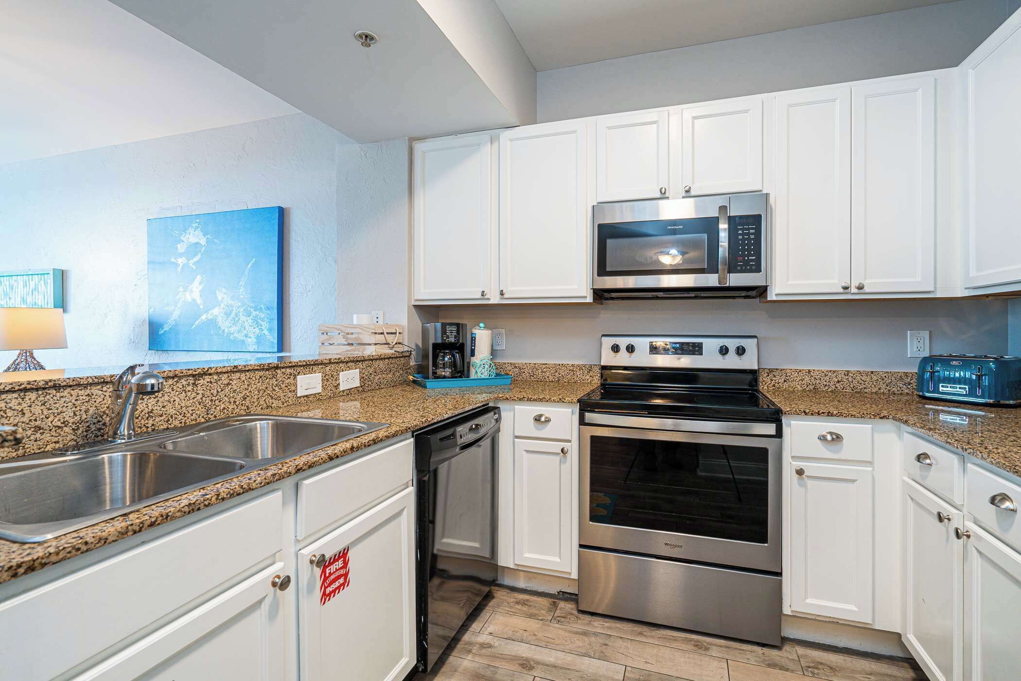 A modern kitchen with white cabinets, stainless steel appliances, granite countertops, and a blue artwork on the wall.