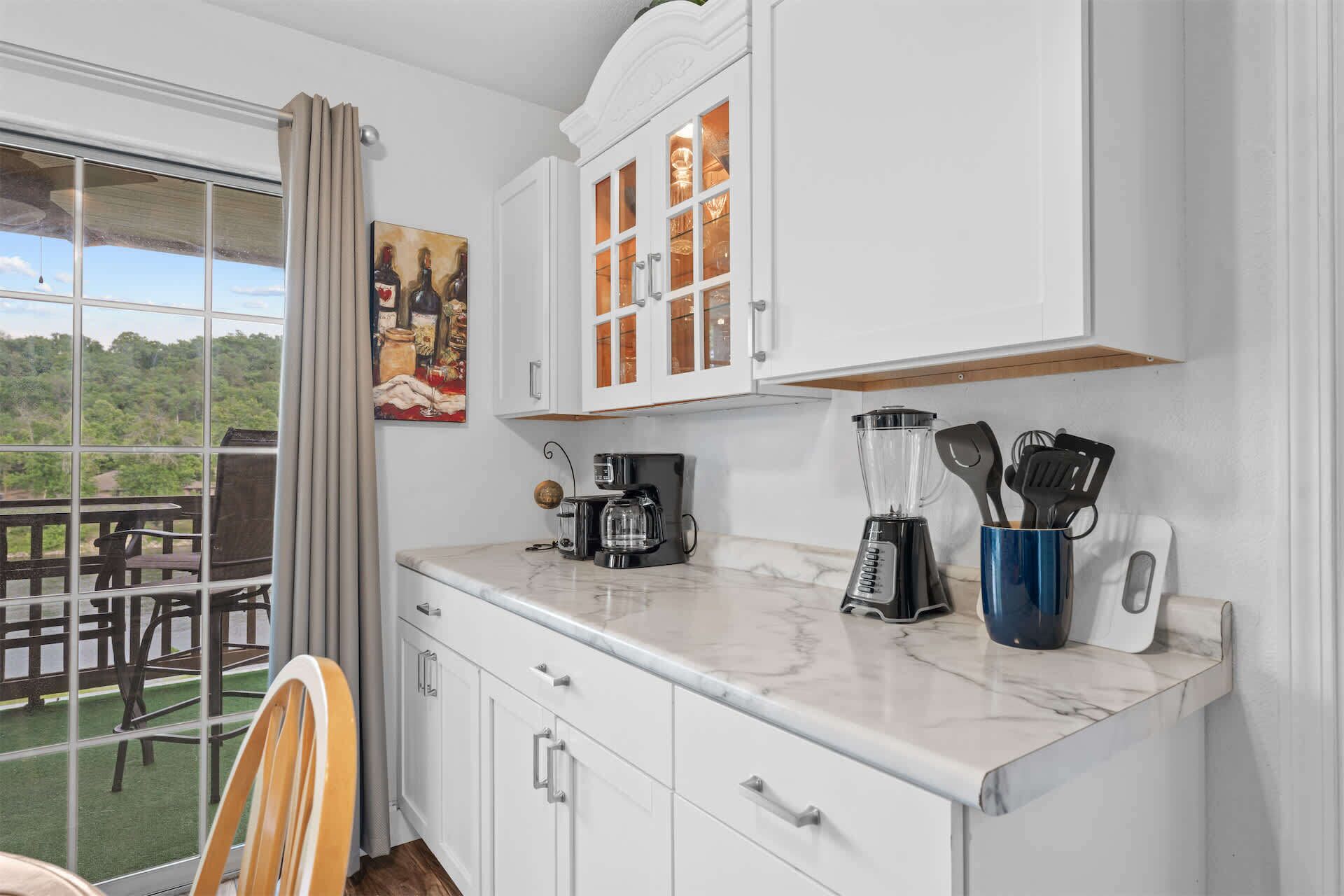 A kitchen with white cabinets, a coffee maker, a blender, and a set of kitchen utensils.