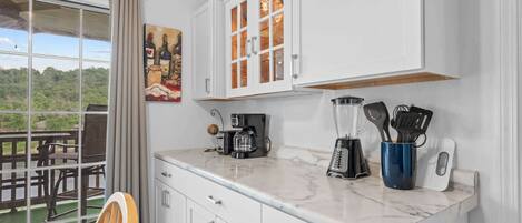 A kitchen with white cabinets, a coffee maker, a blender, and a set of kitchen utensils.