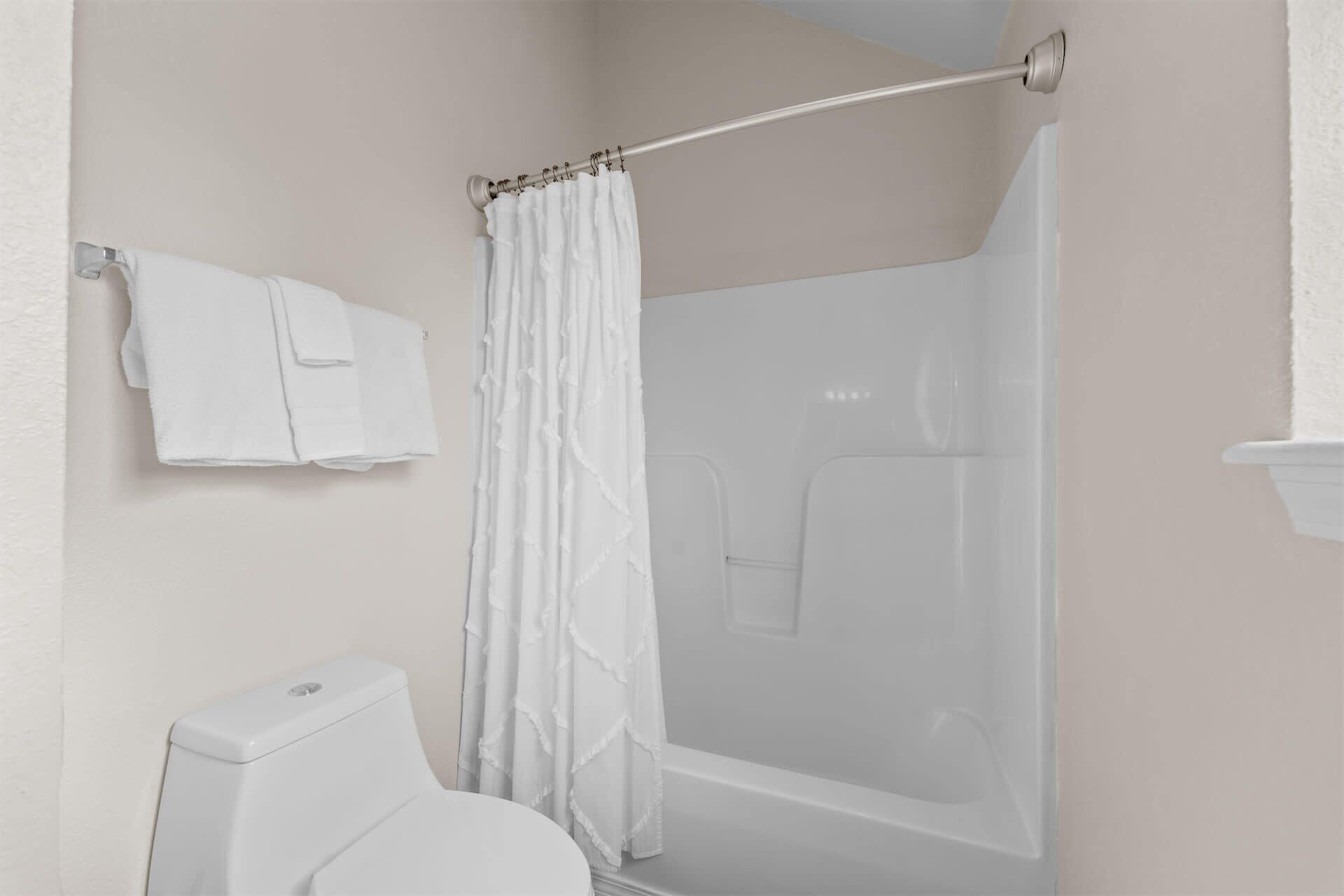 A bathroom with a toilet, a shower with a curtain, and a towel rack with towels.