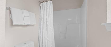 A bathroom with a toilet, a shower with a curtain, and a towel rack with towels.