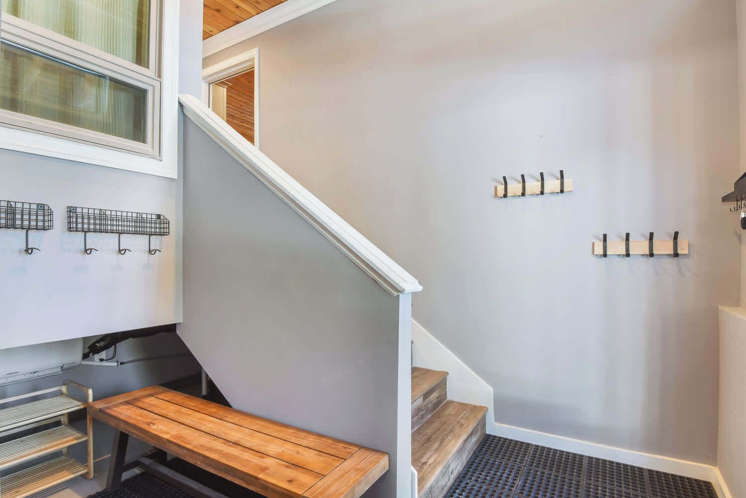 A staircase with a wooden bench at the bottom, a metal rack, and a wall-mounted coat rack.