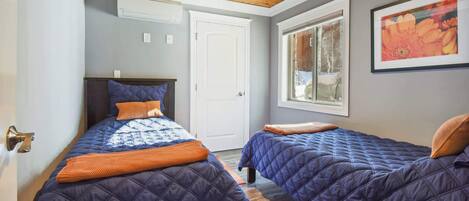 A bedroom with two beds, a wooden ceiling, a window with a view, and a door.
