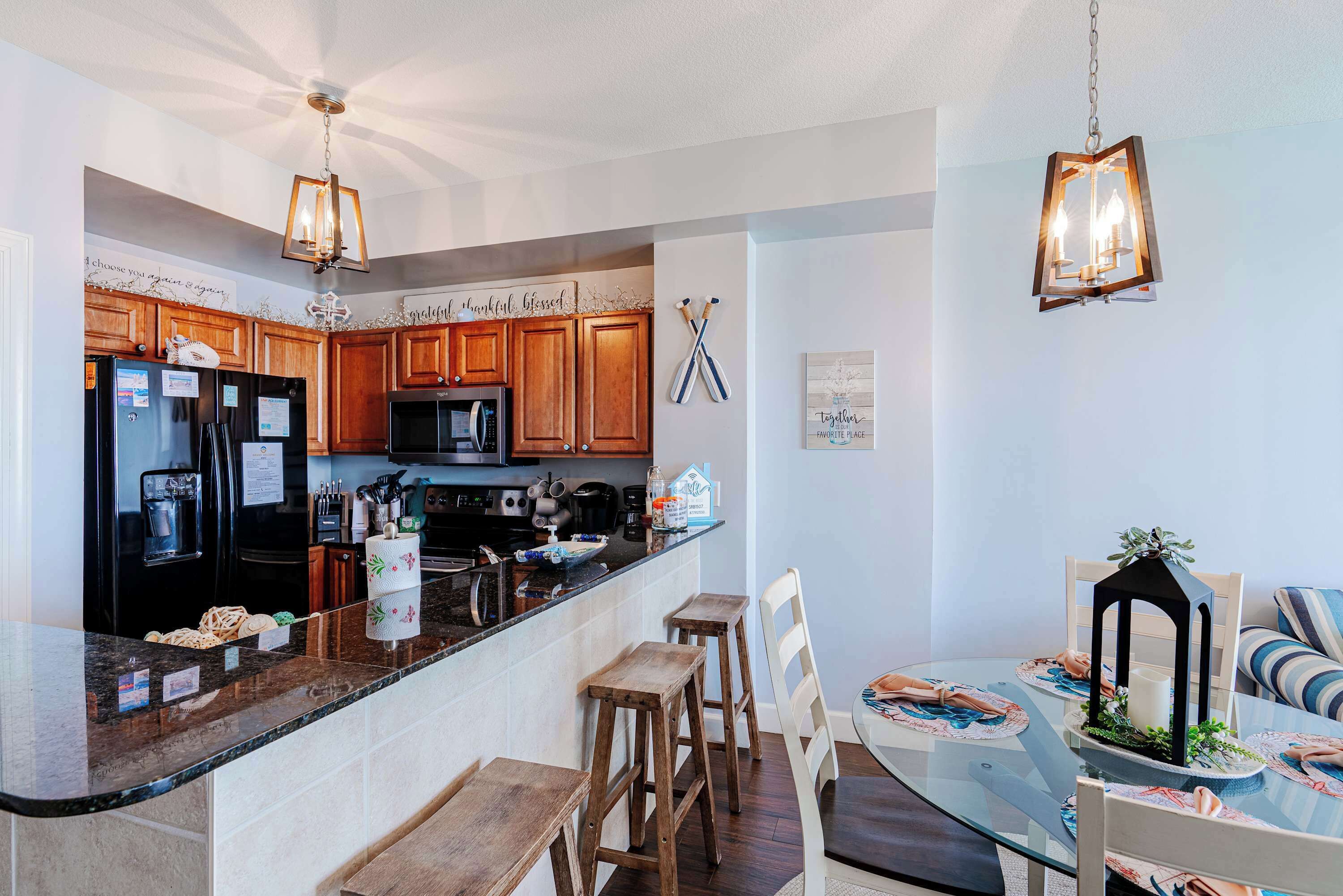 A modern kitchen with wooden cabinets, a black refrigerator, and a dining area with a glass table and wooden chairs.