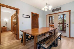 A spacious dining area with a wooden table and benches, wooden doors, and a chandelier.