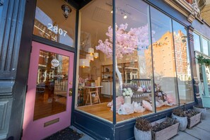 Une boutique avec une porte rose, de grandes vitrines où sont exposés des objets artisanaux et une enseigne indiquant qu’elle est ouverte.
